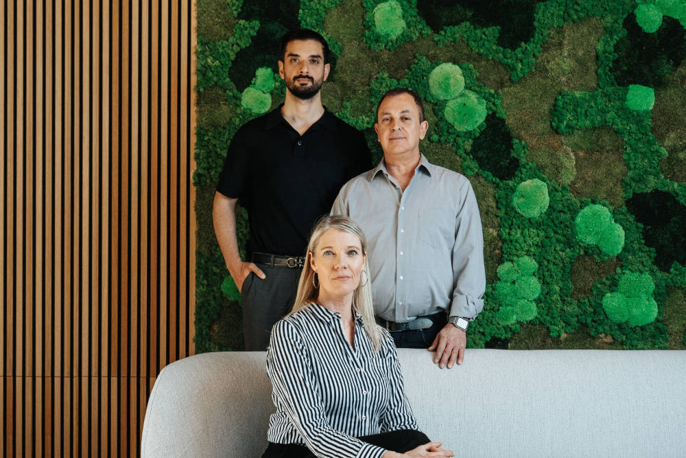 Teamfoto von Akzenta Immobilien: zwei Männer und eine Frau vor einer grünen Mooswand – Partner im Immobilienvertrieb