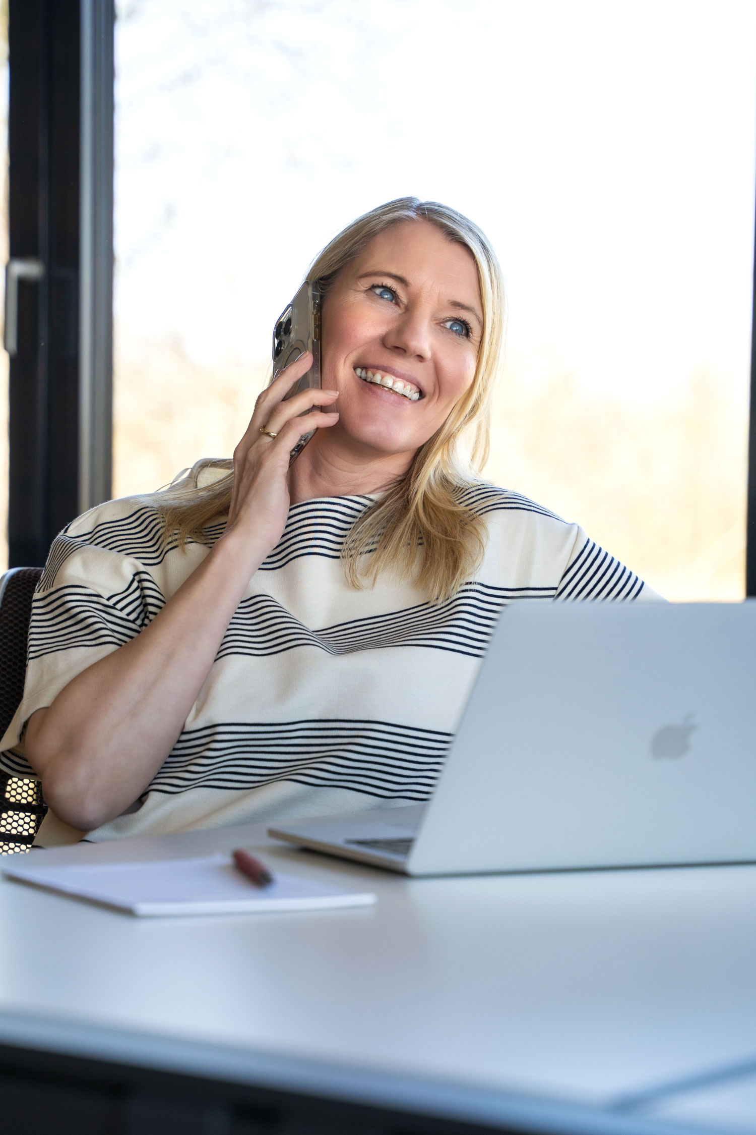 Lächelnde Frau telefoniert im Büro und arbeitet am Laptop – persönliche Beratung bei Akzenta Immobilien